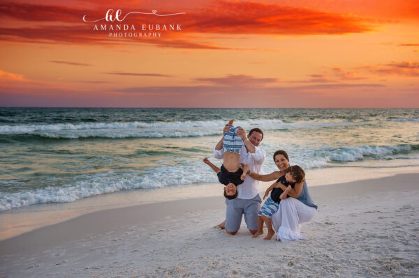 Destin family photographer captures playful family with dad holding baby upside down at sunset