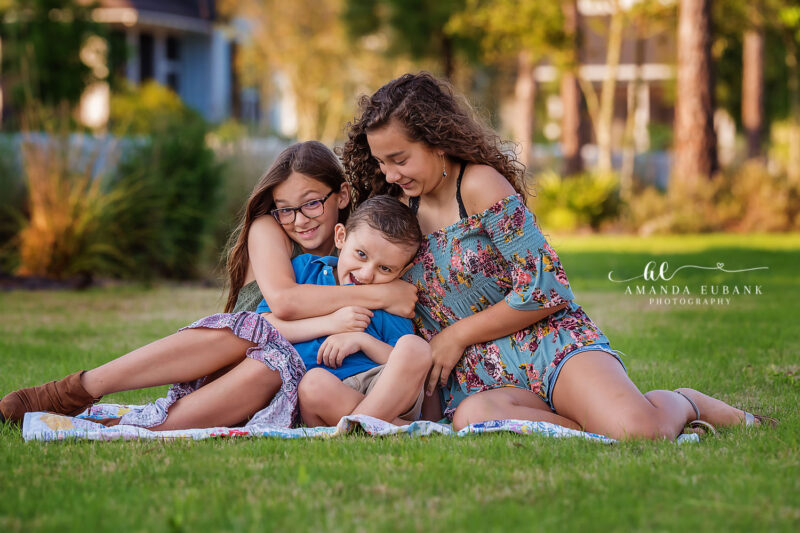 Destin family photographer captures three siblings in group hug on grass with golden hour light